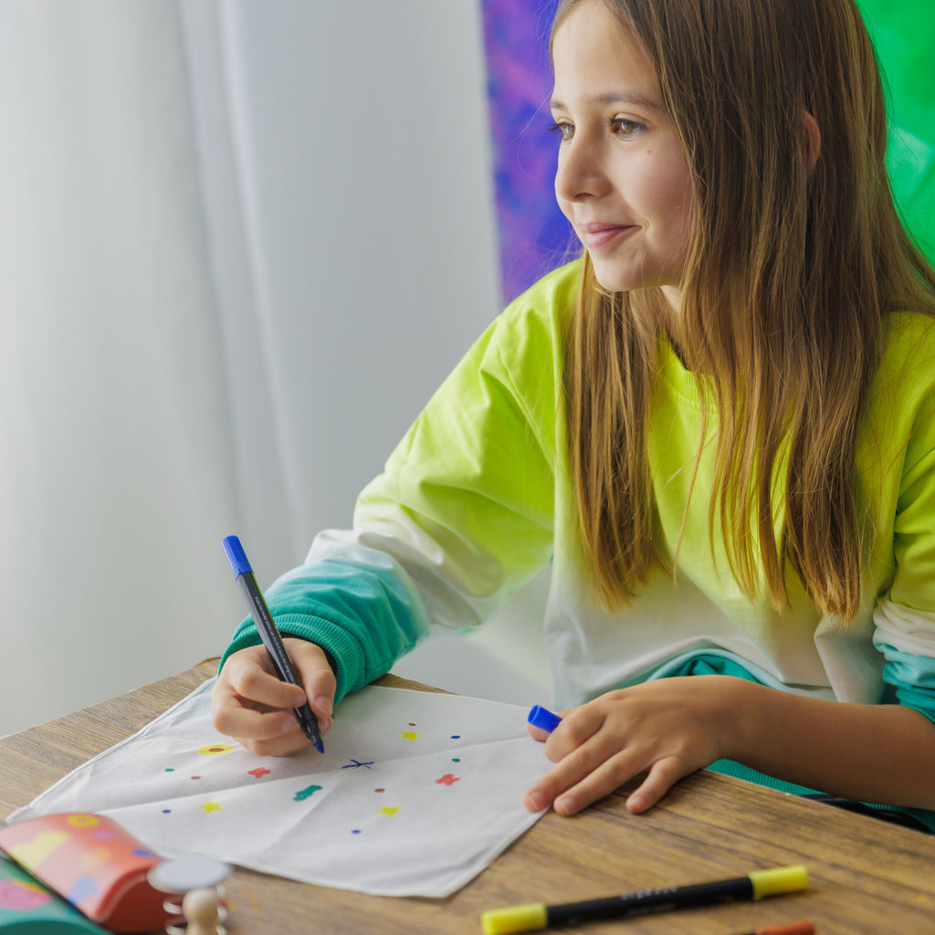 Close-up of a young maker drawing unique patterns on a fabric bandana using colorful textile markers.