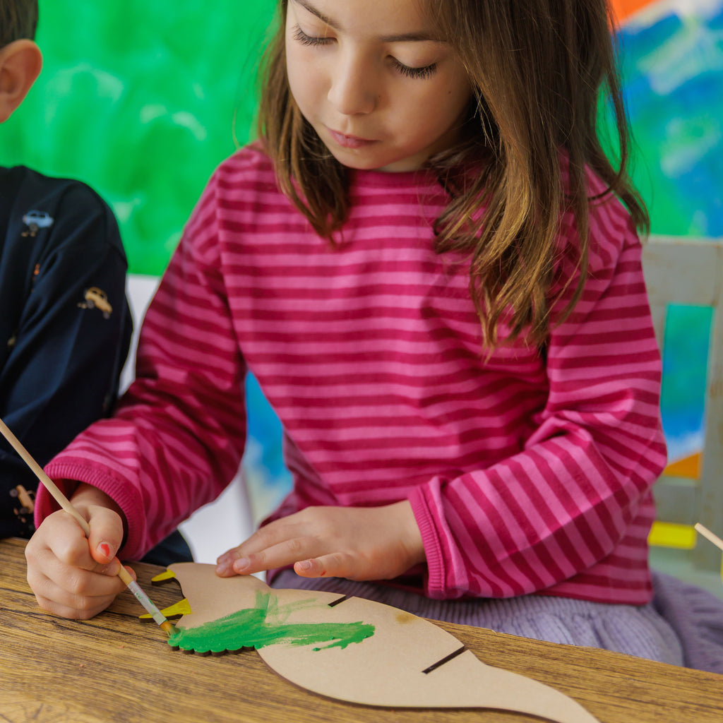 Hours of screen-free fun: a child fully immersed in painting and decorating their own wooden dino skeleton.