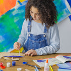 A child painting a wooden whale blue, practicing creativity and color mixing with a Dabble & Co. art kit.