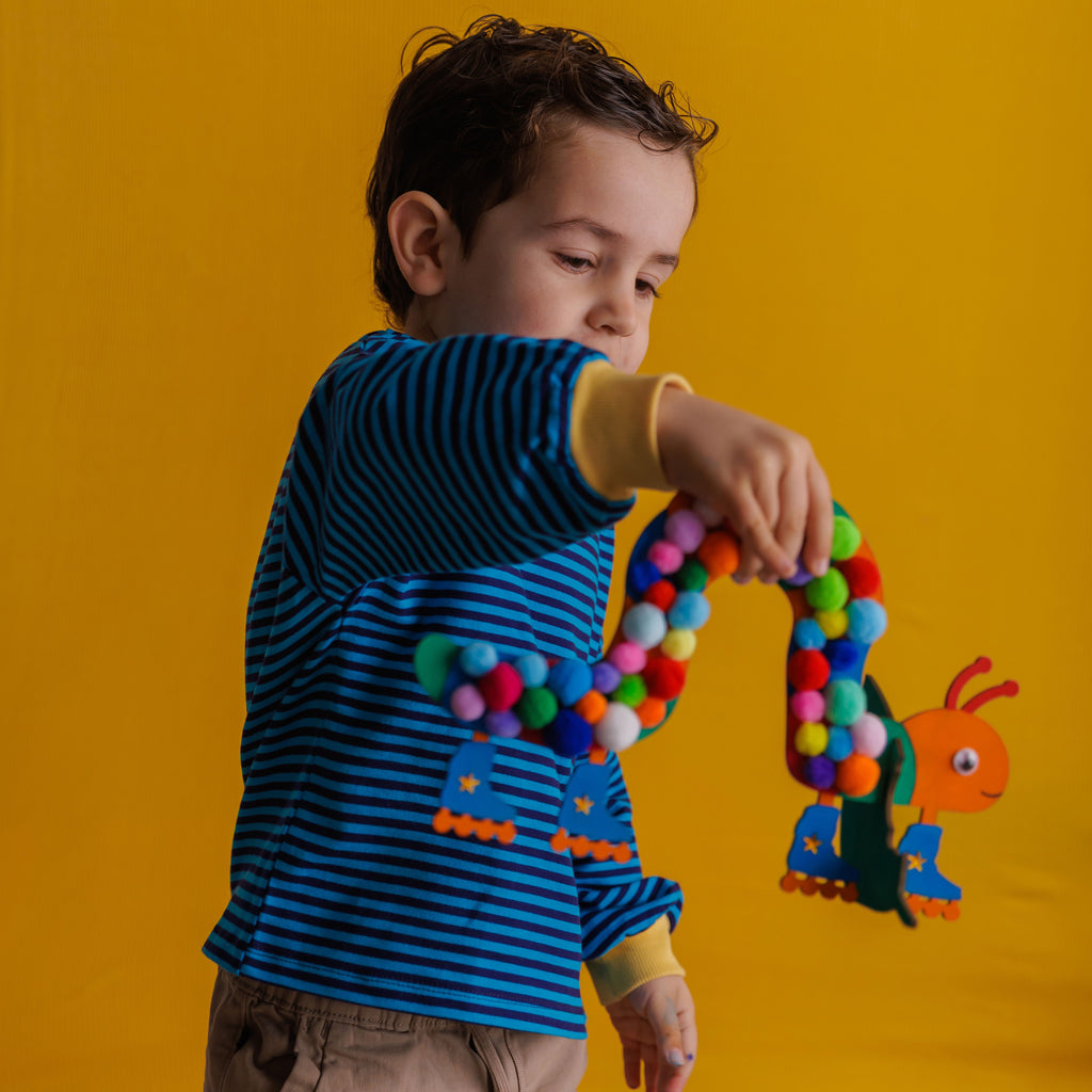 A proud child showing off their finished Disco Caterpillar, complete with pompoms and glittering stars on the wheels.