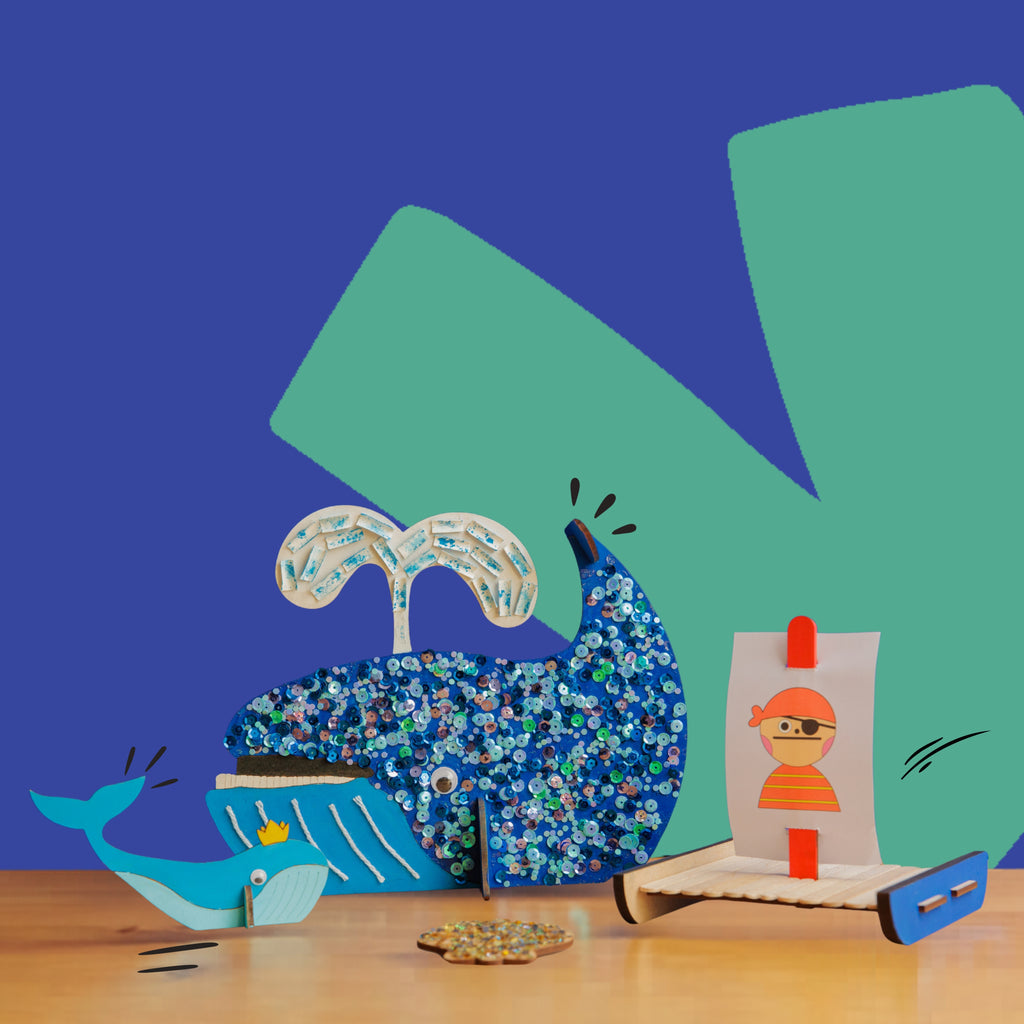 Fiona the Whale craft kit by Dabble & Co. including two wooden whales, a DIY raft with a sail, paint, and glitters.