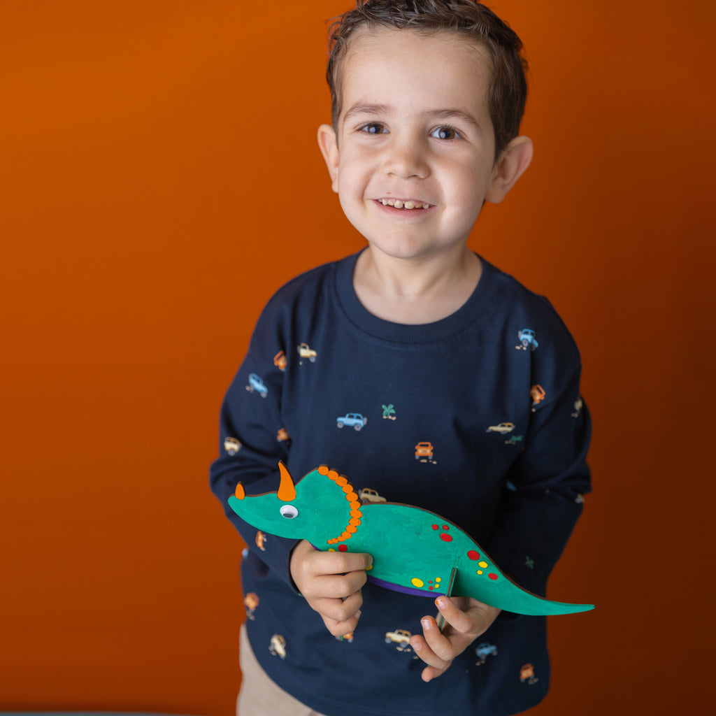 A proud young explorer showing off their hand-painted wooden dino, ready for an adventure in the matching volcano box.