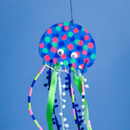 The finished Jelly! the Jellyfish project: a colorfully painted wooden jellyfish with flowing tentacles made of silk ribbon, pompom trim, twine, and straws.