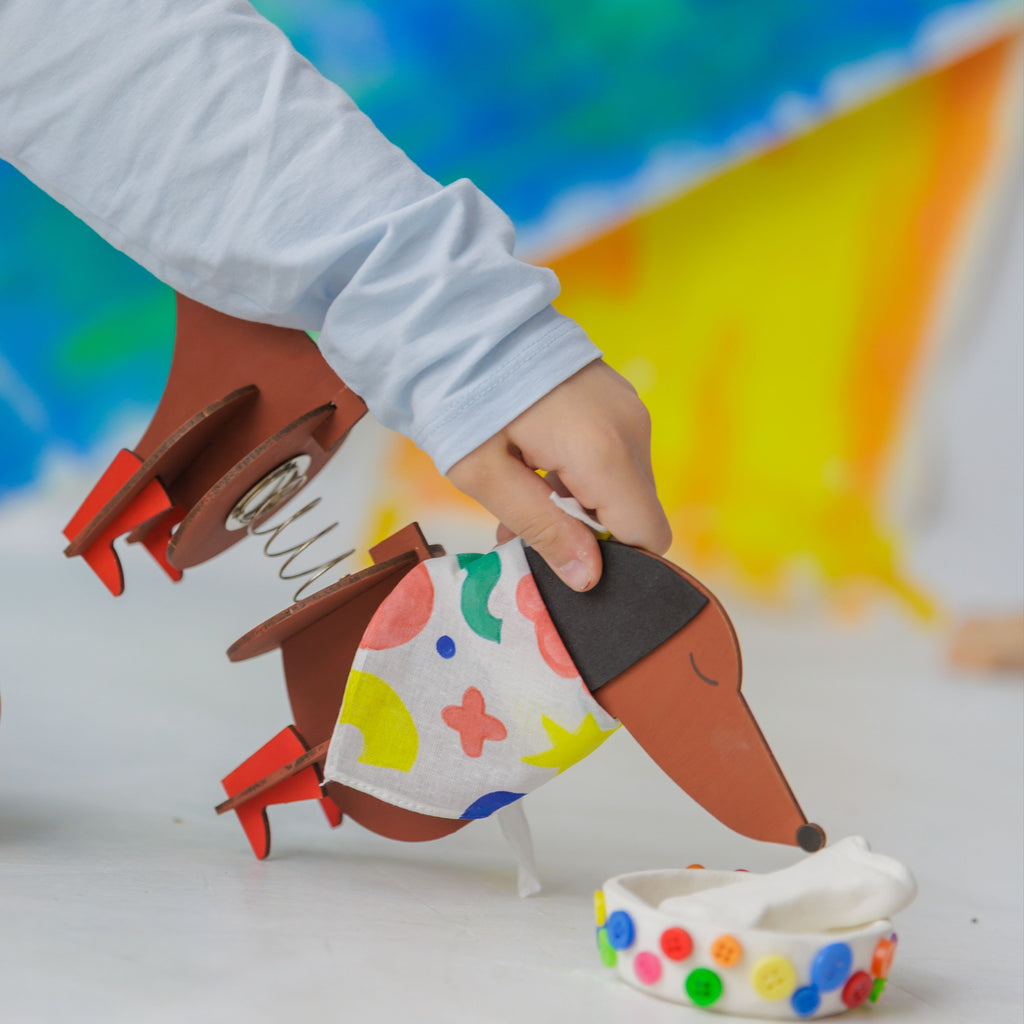 Dabble & Co. Dot the Dog complete craft kit: an all-in-one DIY set with a wooden dog, foam ears, fabric bandana, textile markers, air-dry clay, and buttons.