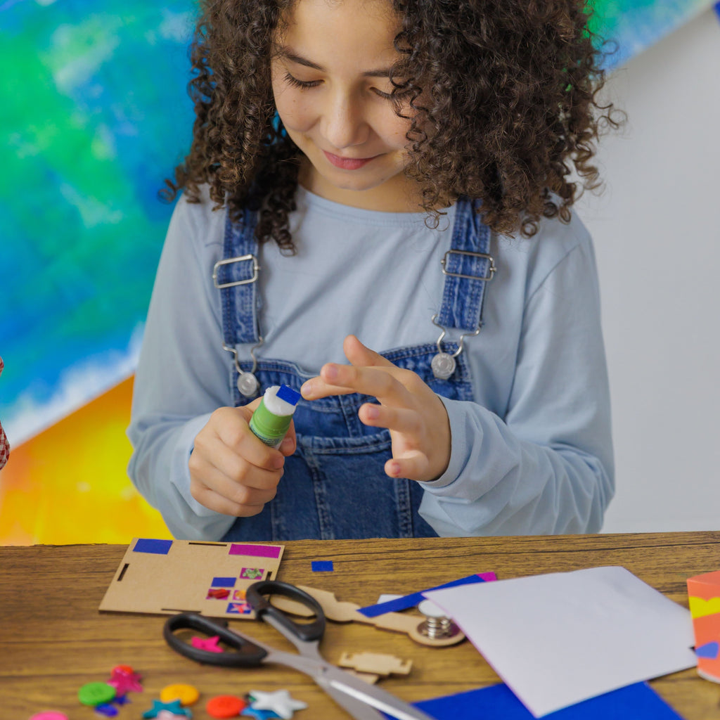 Cutting and gluing glitter paper to personalize Robbie the Robot with unique patterns and shapes.