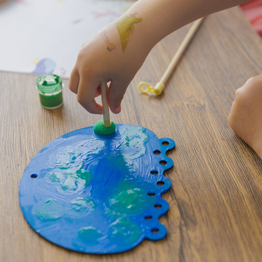 Creative techniques for kids: using sponge brushes to stamp textures and patterns onto the painted wooden jellyfish.