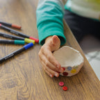 Carefully placing colored buttons onto a clay dog bowl to create a personalized mosaic effect.