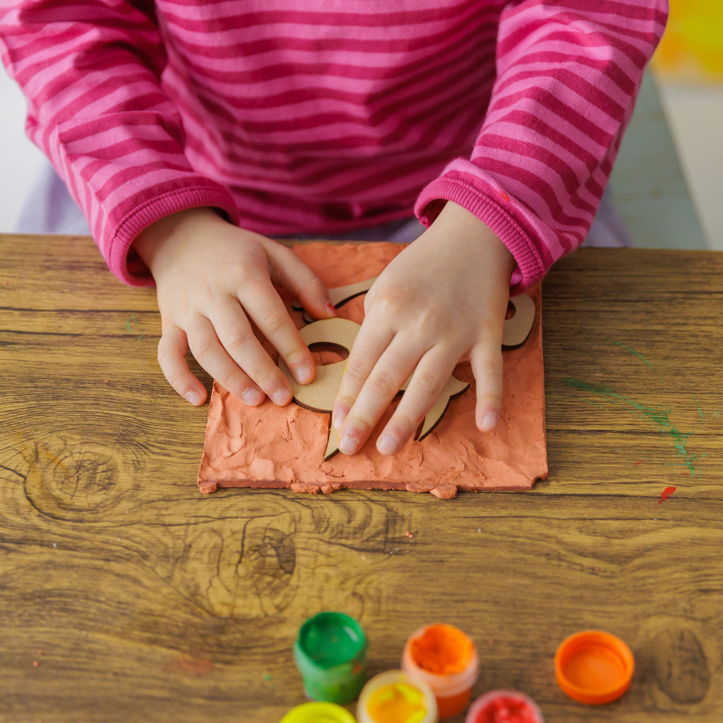 Close-up of the crafting process making bone imprints in soft terracotta clay for an authentic fossil look.