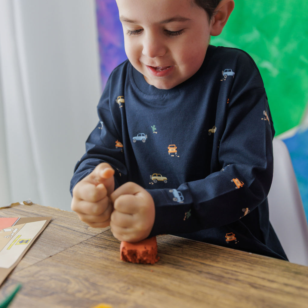 Small hands modeling terracotta air-dry clay to recreate an archeological dig site within the dinosaur craft kit.